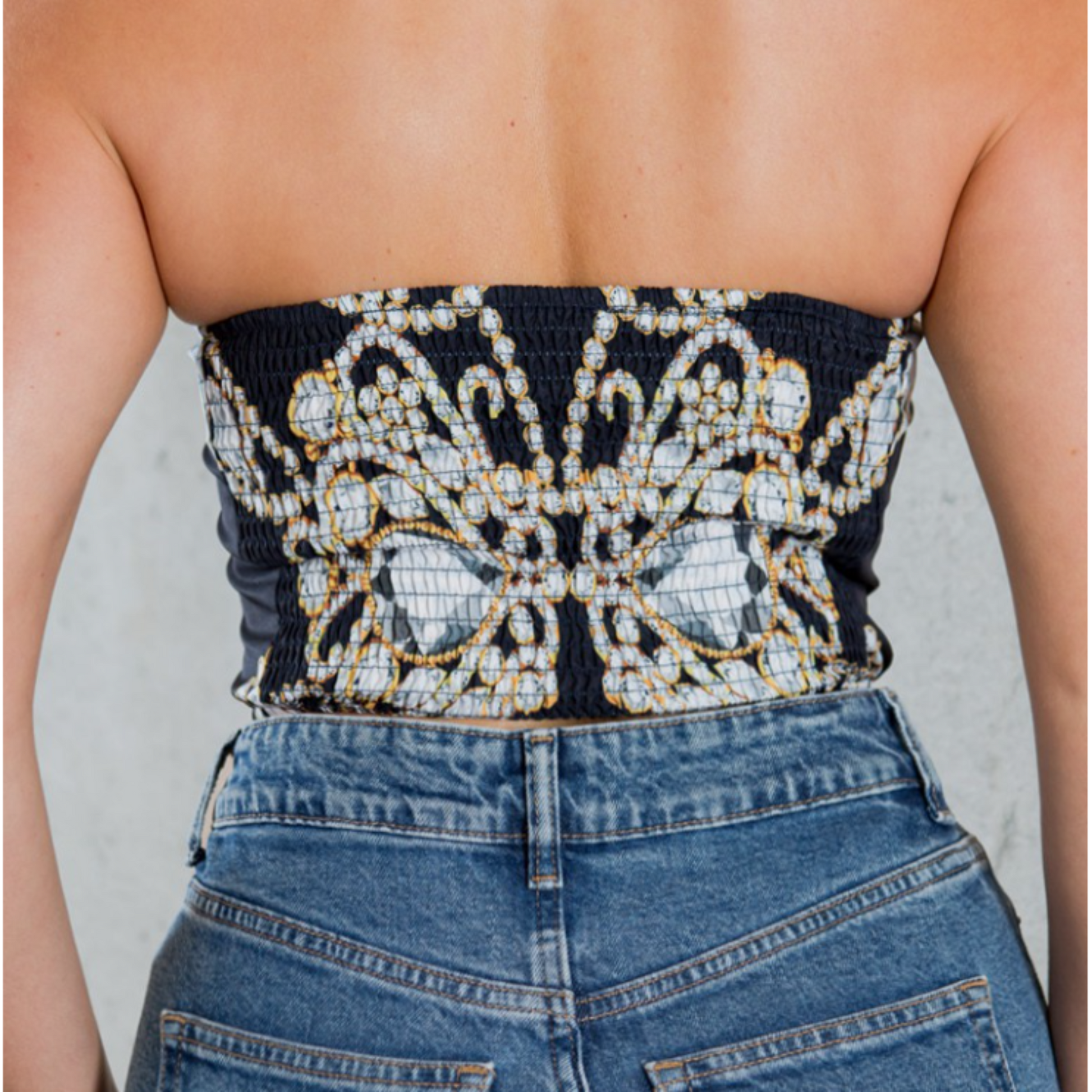 Person wearing a strapless top with intricate beadwork and blue jeans.