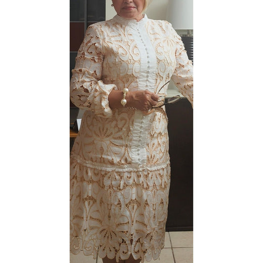 Woman wearing a long sleeve white lace dress with buttons and a belt, standing indoors.