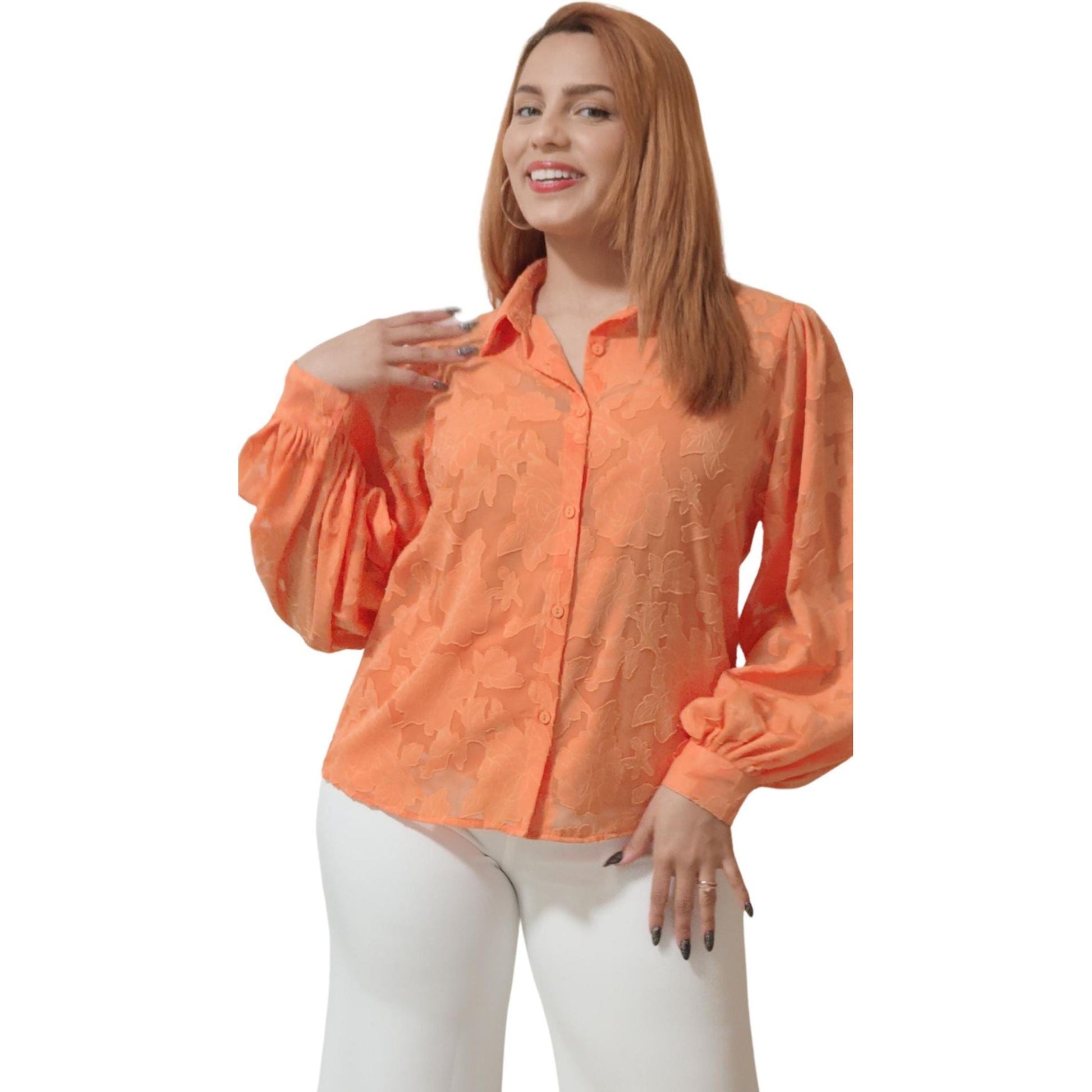 A woman wearing an orange blouse with a textured woven pattern and a traditional shirt collar, paired with white pants and accessorized with a smile.