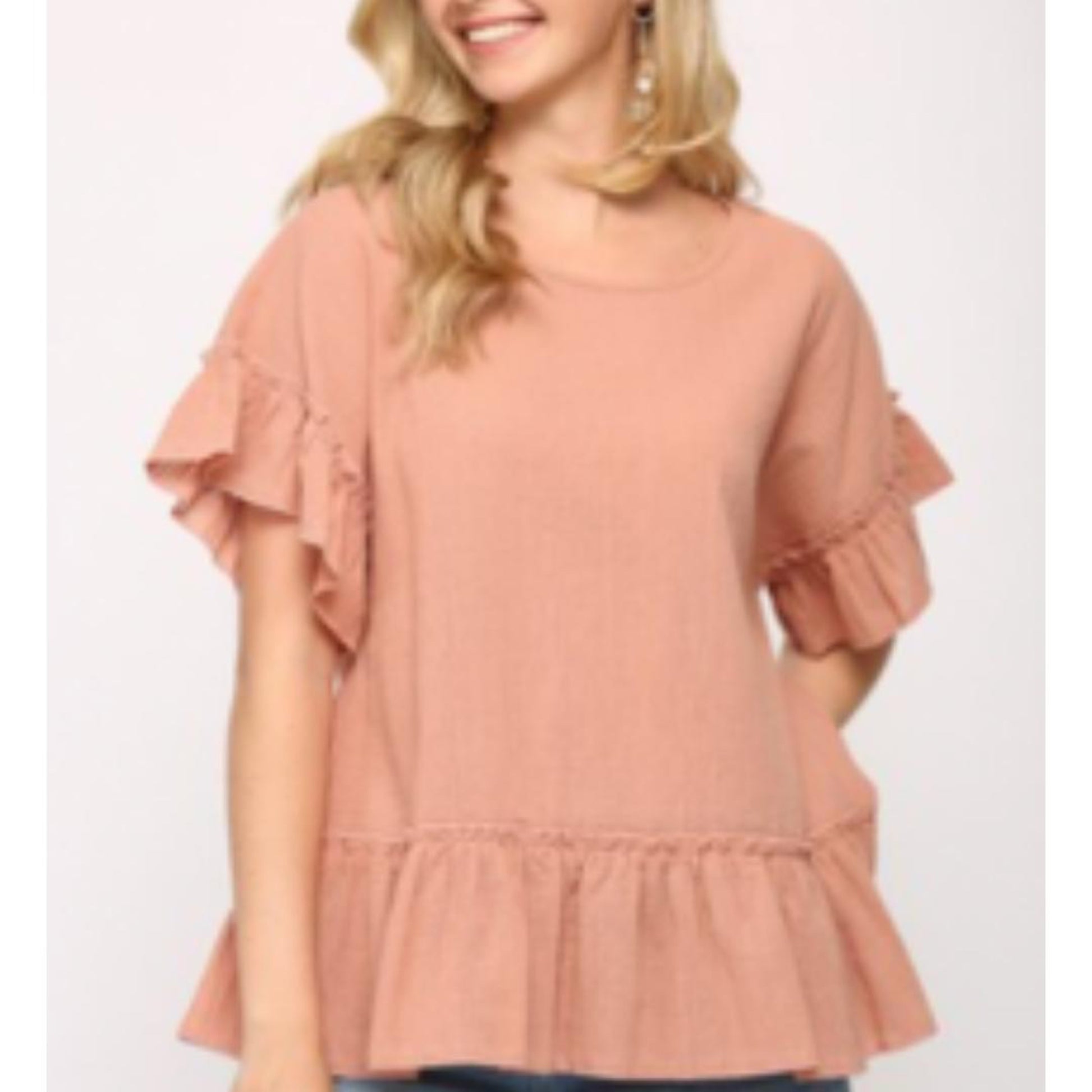 A female model wearing a beige tassel tie top with a round neckline and three-tier tassel detail, paired with blue jeans.