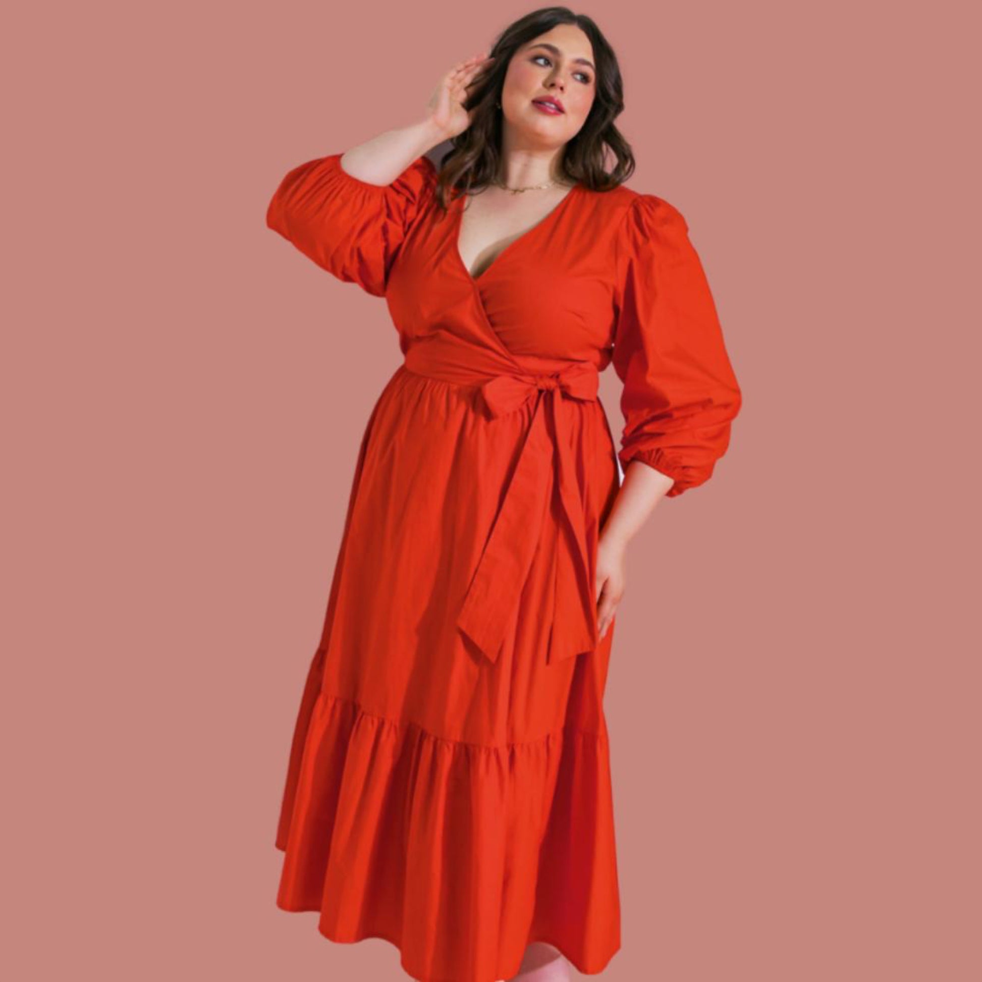 A woman wearing a red, midi-length dress with a surplice neckline, long sleeves, and a ruffled hemline. The dress features a true wrap with a side tie.