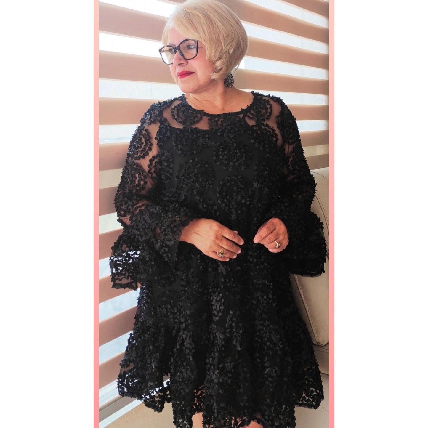 A woman wearing a black, frilled hem flounce sleeve sheer trapeze dress with lace detailing.