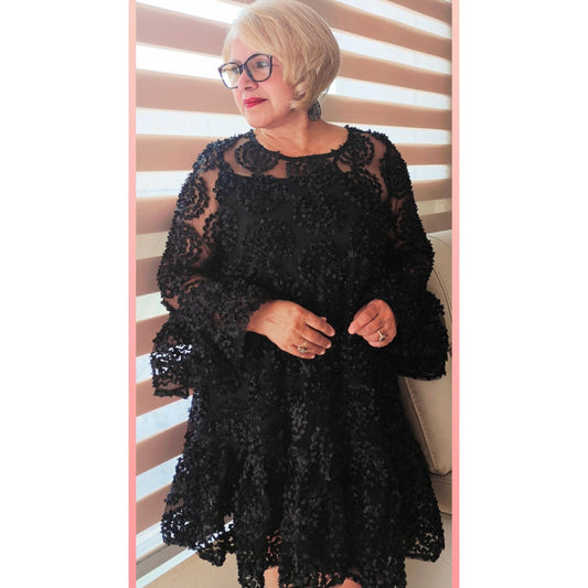 A woman wearing a black, frilled hem flounce sleeve sheer trapeze dress with lace detailing.