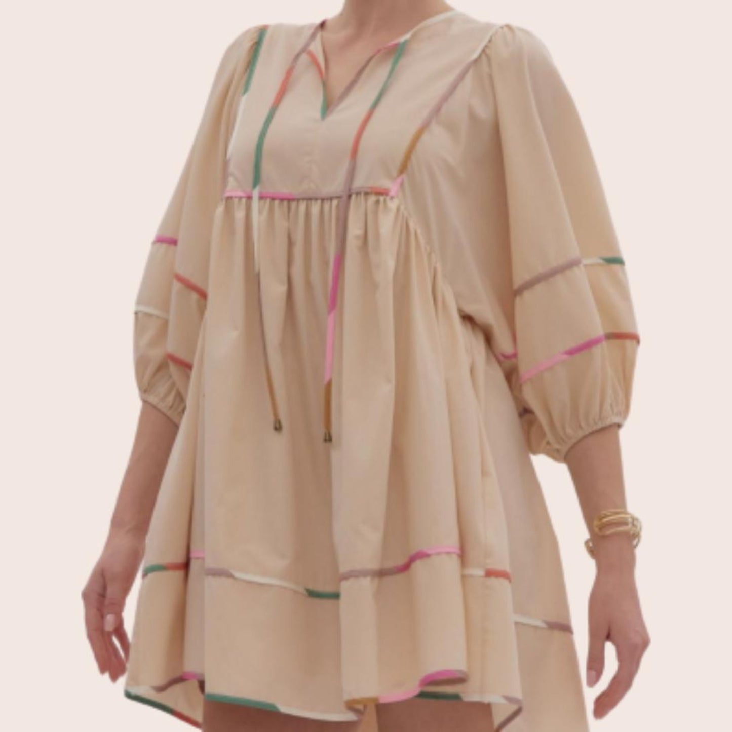 A bohemian-style dress in beige with colorful stripes, featuring three-quarter length puffed sleeves and a drawstring at the top.