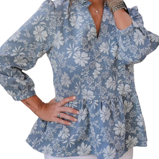 A woman wearing a blue floral peplum top with a V-neckline and a round necklace.