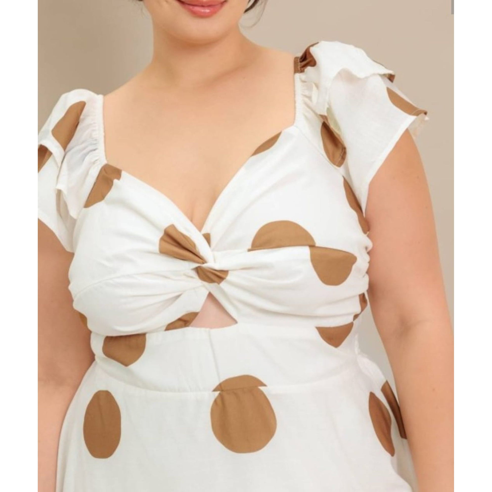 White dress with brown polka dots and cut-out shoulders on a neutral background