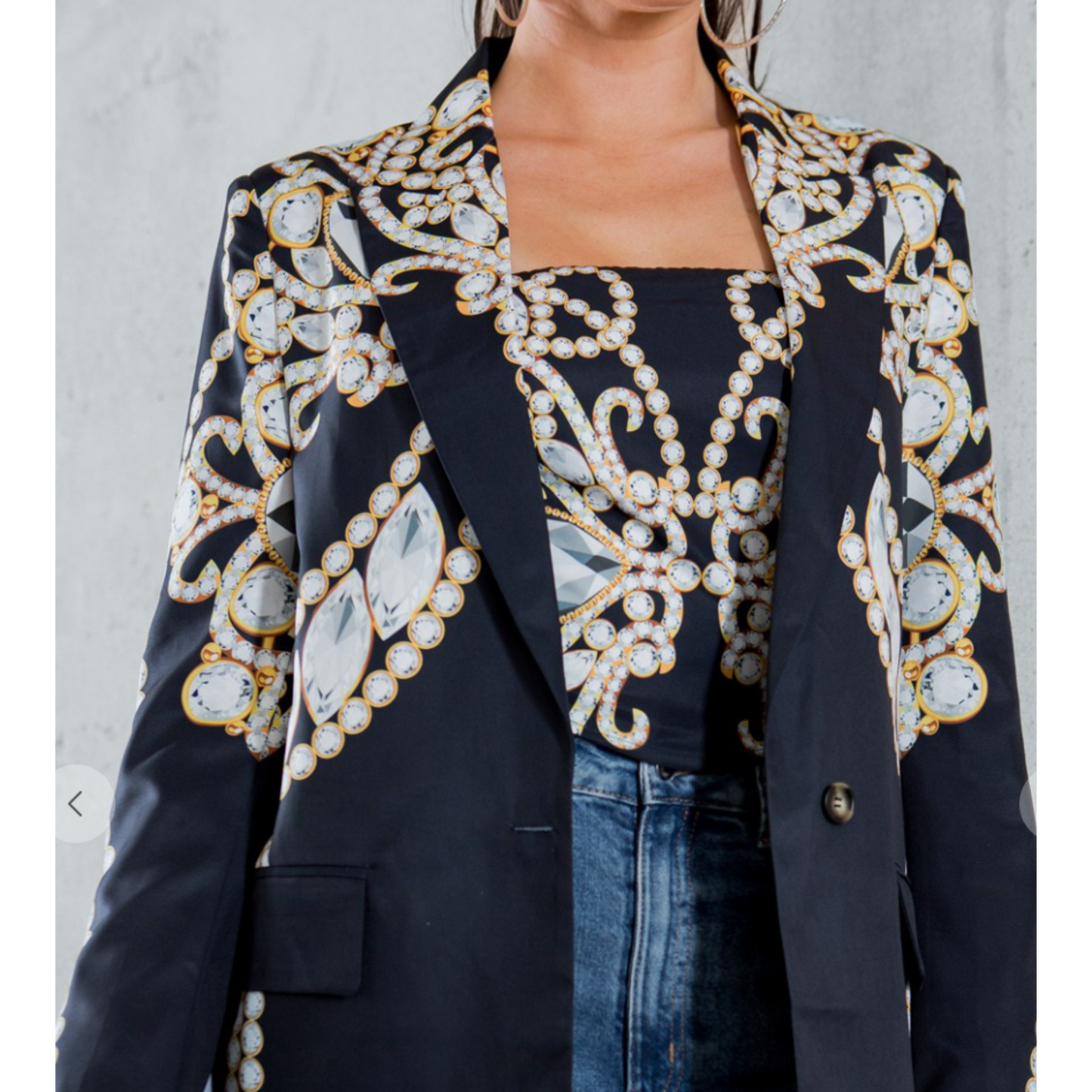 Navy blazer with gold and white embellishments worn by a person against a gray background