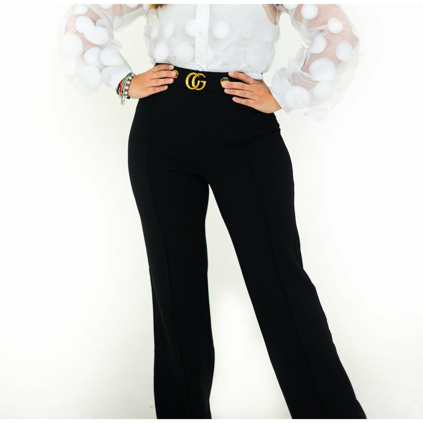 A person wearing black flare pants with a white blouse, featuring a belt with a gold buckle.