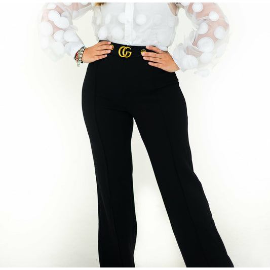 A person wearing black flare pants with a white blouse, featuring a belt with a gold buckle.