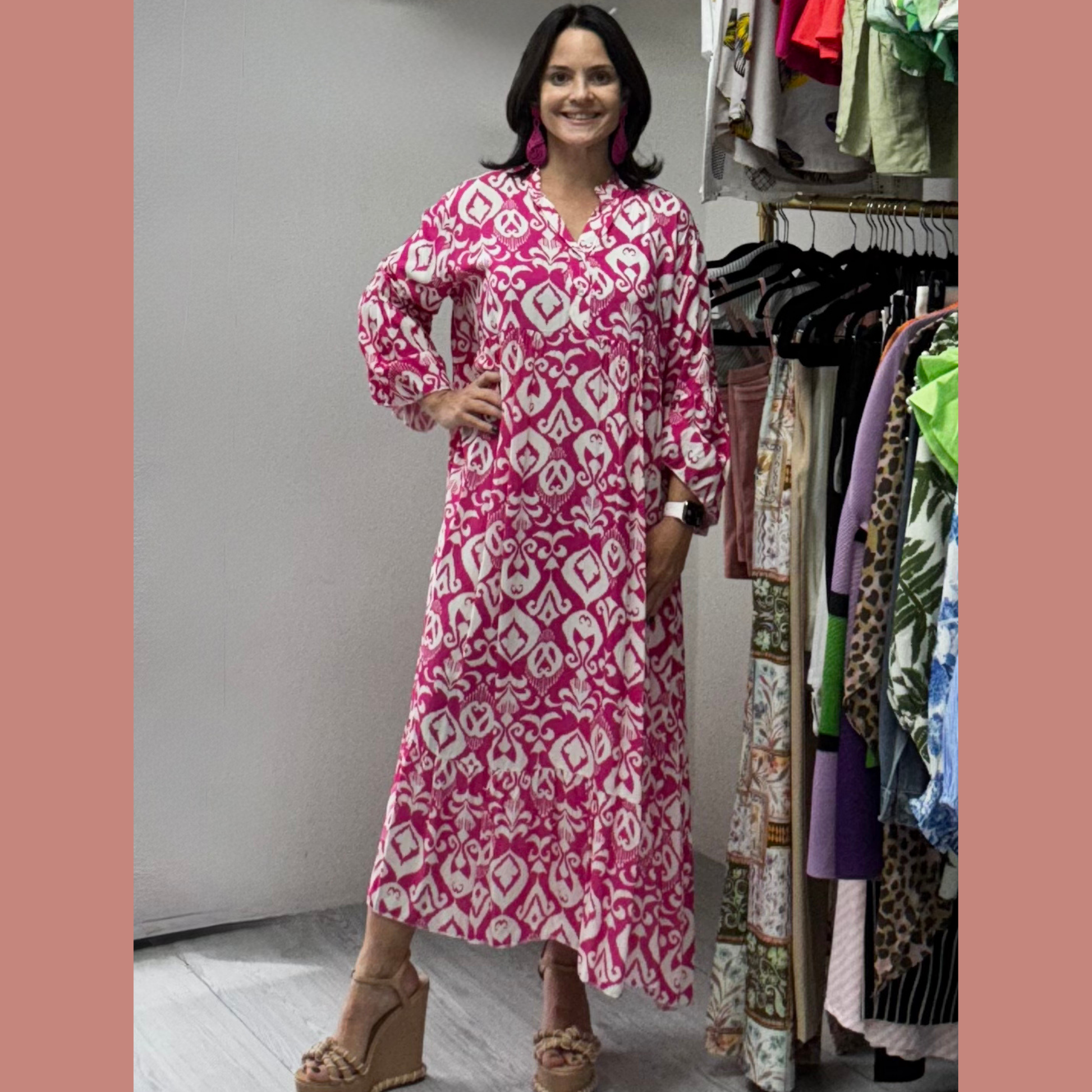 Woman wearing a pink and white patterned dress standing in front of a clothing rack.